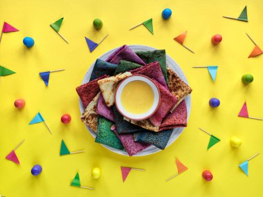 Gökkuşağı partisi, masa kurulumu. Ballı canlı krep tabağı. Parti masası, çeşitli renklerde bayraklı sarı masa örtüsü. Gökkuşağı kapsayıcılığın sembolü, LGBT gururu.