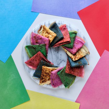 Katmanlı gökkuşağı kağıdının arka planında gökkuşağı renginde krep tabağı. Düz, canlı renkler, kırmızı, mor, turuncu, yeşil, sarı. Yaratıcı, canlı, kalın renkler, gıda konsepti..