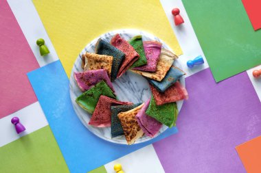 Katmanlı gökkuşağı kağıdının arka planında gökkuşağı renginde krep tabağı. Geometrik düz, kırmızı, mor, turuncu, yeşil, sarı renkler. Tahta figürler. Yaratıcı, canlı, kalın renkler, gıda konsepti..