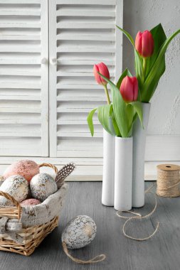 Springtime Easter decorations on rustic wooden table. Easter eggs in basket, quail feathers, pussy willow, red tulips, hemp cord. Shabby chic eco friendly Easter decor using natural materials.