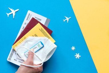 COVID-19 kısıtlamaları sırasında yeni normal bir seyahat, mavi sarı kağıdın üzerinde düz bir şekilde yatıyordu. Alman pasaportu, uçuş kartı ve pp2 tıbbi maskesi üzerinde yapılan son negatif koronavirüs testi. Uçak siluetleri.