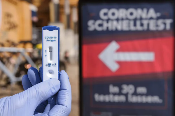 Berlin, Germany - April 11, 2021: Hand in glove hold Express COVID-19 test in front of advertising for quick testing in Berlin Prenslauerberg. Schnelltest means rapid corona test in German language.