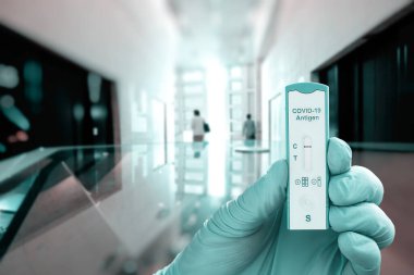 Coronavirus enfeksiyonunu soyut geometrik mimari arka planda test etmek için eldiven tutarak COVID-19 antijen testi yapın. Panoramik pankart resmi.