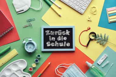 Zuruck in die Schule ya da Almanca okula dönmek demek. Corona, ikna edici ve hızlı testler, tıbbi maske, sabit duruş. Bilgisayar klavyesi. Katmanlı renkli kağıt zemin üzerinde düz uzandı.