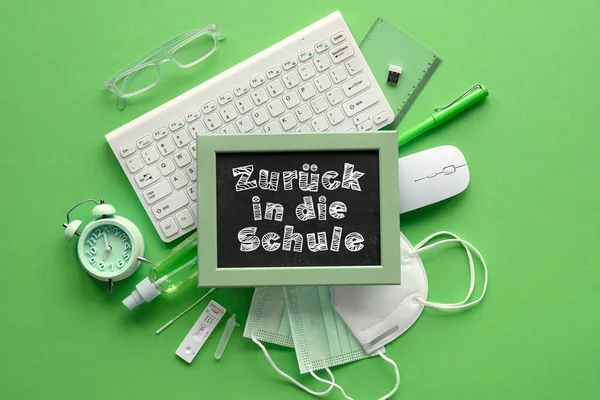 Zuruck in die Schule means Back to school in German. School reopening during corona pandemic restrictions, quarantine. Covid antigen quick tests, medical mask, stationary. Monochrome green flat lay.