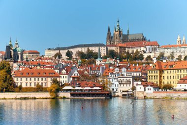 Mala Strana 'nın tarihi binalarının turuncu çatılarına sahip Aziz Vitus Katedrali ve Prag Şatosu, Çek Cumhuriyeti' nin Prag kentindeki aydınlık bir yaz gününde Vltava nehrine yansıdı..