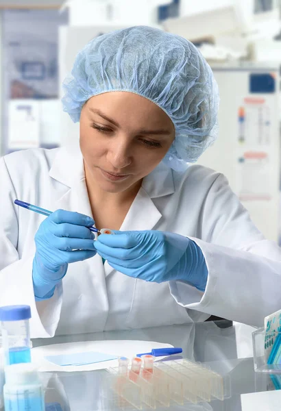 製薬業界の女性技術者が研究室で働いてる ヨーロッパの女性 保護手袋の若い大人 帽子および白いガウンはサンプルチューブを扱う 研究室の内部に焦点を当ててる バイオテクノロジー研究 — ストック写真