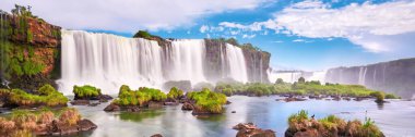 Iguazu waterfalls in Argentina. Panoramic view of many majestic powerful water cascades with mist and clouds. Panoramic image of Iguazu valley with grass and stones in calm water. clipart