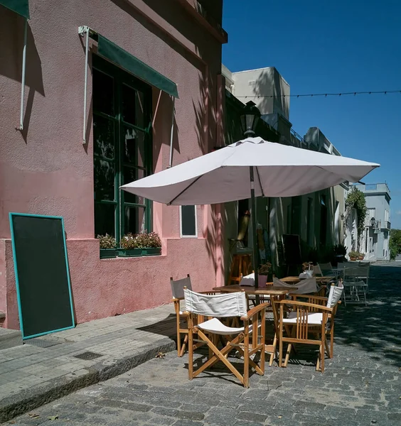 empty table in an outdoor restaurant in the old town in Colonia Uruguay, the tables are shaded with umbrellas. The street is paved with old cobble stones