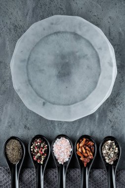 Seramik oryantal kaşıklarda çeşitli baharatlar ve koyu gri kaselerde çimdik. Arka planda tekstil havlusu. Plakasında kopyalama alanı olan düz bir yer. Çeşitli kuru otlar, biber, tütsülenmiş tuz, kırmızı biber, kekik..