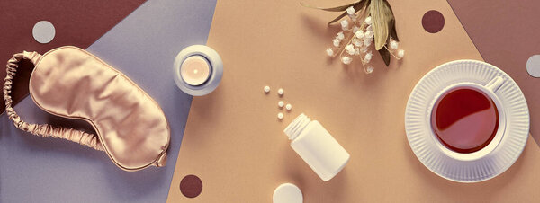 Quality of sleep banner. Sleep mask, sleeping pills, scented candle and cup of calming tea. Two tone layered silver, gold, beige and brown paper flat lay, top view. Lily of the valley flowers.
