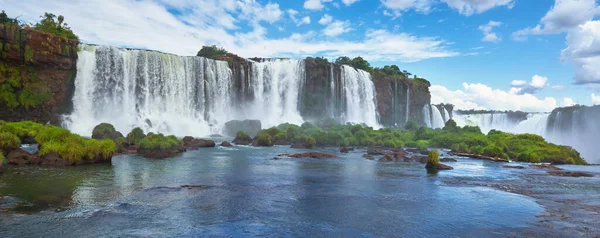 Iguazu waterfalls in Argentina, view from above. Panoramic view of many majestic powerful water cascades with mist. Panoramic image with reflection of blue sky with clouds.