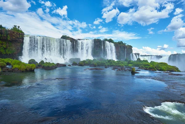 Iguazu waterfalls in Argentina, view from above. Panoramic view of many majestic powerful water cascades with mist. Panoramic image with reflection of blue sky with clouds.