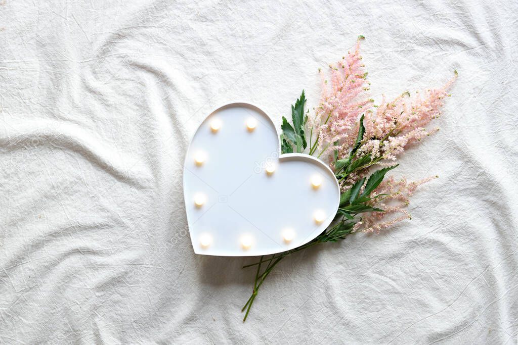 Heart lightbox and wild flowers . Flat lay on off white textile. Natural materials, environment concious, low impact, eco friendly lifestyle concept. Pale pink Prachtspiere flower.