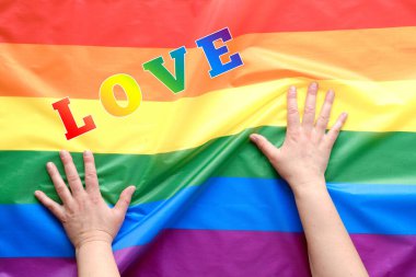 Mutlu Gurur Ayı. Basit, asgari LGBT gurur dekoru. Çizgili bayrağın üzerinde gökkuşağı renginde tırnakları olan insan elleri. Pankartta 