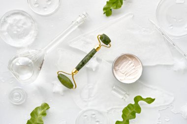 Kendi ellerimle nemlendirici ve yeşil yeşim taşlı buz parçalarıyla yuvarladım. Beyaz arka planda egzotik yeşil eğreltiotu yaprakları ve su damlaları var. Yüz masajı, el yapımı kozmetik..