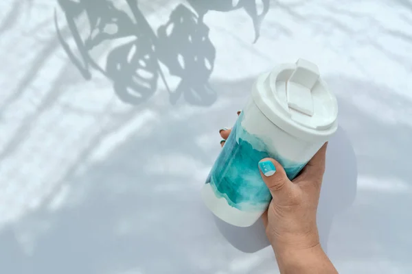 手与零浪费的咖啡杯去 绿松石修指甲与杯子上抽象的蓝色绿色图案相配 时尚可重复使用的生态咖啡杯 盖在手 — 图库照片