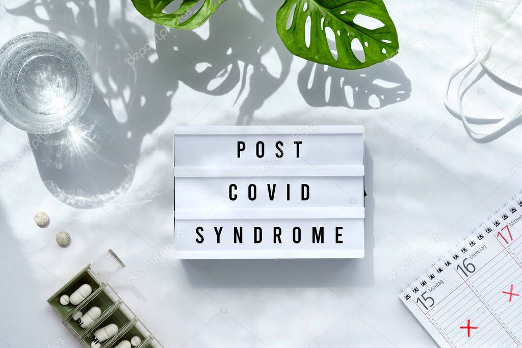 Text Post Covid Syndrome on light box in hand. Long Covid tail awareness design. Off white background with trendy monstera leaves and long shadows. Flat lay, top view overhead.