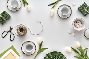 Çay fincanları, beyaz laleler, paketlenmiş hediyeler ve el sanatları araçları ile Paskalya düzlem düzenleme boş beyaz merkez etrafında düzenlenmiş metin ve başlık veya sosyal medya için mevsimsel biçimlendirme