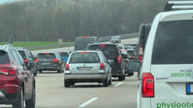 Berlin, Almanya 11 Nisan 2025: Gün içinde Berlin otoyolunda trafik sıkışık, şeritler halinde arabalar ve kamyonetler, ağaçlık yol kenarına doğru yavaşça ilerleyen araçlar ve kuyruk oluşturan trafik ışıkları açık.