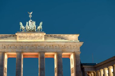 Brandenburg Kapısı şafak vakti aydınlanıyor. Quadriga heykeli neoklasik sütunlar ve derin mavi gökyüzüne karşı sıcak mimari aydınlatma ile aydınlanıyor. Sabahın erken saatlerinde Berlin 'in simgesi ve tarihi şehir atmosferini yakalıyor.