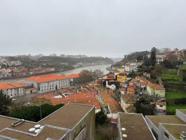 Porto, Portekiz - 16 Şubat 2026: Bulutlu kış gökyüzü ve hafif yağmur Douro Nehri boyunca şehir çatılarını ve tepe kenarlı mahalleleri, kırmızı kiremitli çatıları ve nemli terasları görünür kılarken alçak bulut uzak ufuk çizgisi kontrastını azaltır