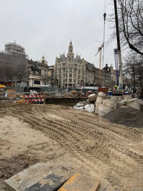 Porto, Portekiz - 16 Şubat 2026: İnşaat alanı, kış yağmuru sırasında çamurlu araç rayları ve havuz suyu ile merkez meydanı işgal etmektedir. İşçiler ve bariyerler erişimi kontrol ederken, Güzel Sanatlar binaları ve vinçler siteyi gözden kaçırıyor.