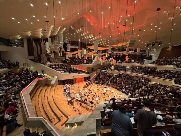 Berlin, Almanya 15 Aralık 2025: Sahnede konser veren orkestrayla dolu konser salonu ve akşam performansı sırasında özel bal peteği tavan ışıklandırması altında birden fazla balkon ve katlar arasında oturan seyirci.