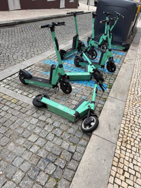 Porto, Portekiz - 15 Şubat 2026: Paylaşılan elektrikli scooterlar, Porto şehir merkezindeki kış günlerinde kaldırım döşemeleri ve çöp konteynırlarının yanında, kaldırım taşı caddesindeki parke edilmiş mavi park alanında devrilmiş olarak yatıyor.