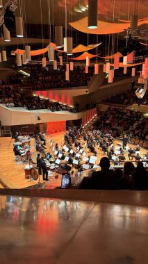 Berlin, Almanya - 15 Aralık 2025: Filarmoni Orkestrası Berlin 'de sahne alıyor, modern konser salonu, müzisyenler ve orkestra şefi görünür, katlar ve balkonlarda seyirci, askıya alınmış akustik şaşkınlıklar ve sıcak sahne ışıklandırması