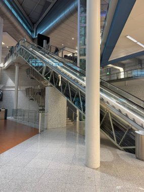 Porto, Portekiz - 16 Şubat 2026: Porto Havaalanı 'nın iç görünümü yürüyen merdivenleri, camlı asansör boşluğunu, yapısal sütunları ve sabah operasyonları sırasında birkaç yolcu arasında hareket eden yolcuları gösteriyor