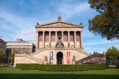 Berlin, Almanya 2 Ekim 2015: Müze Adası 'ndaki Altes Müzesi cephesi mavi gökyüzünün altında, merdivenlerde ziyaretçiler ve girişte binicilik heykeli bulunuyor. Kırmızı bayraklar merdivenlerden ve vinçler binanın arkasından yükseliyor..