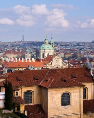 Aziz Nicholas Kilisesi Kubbesi, Barok ön cepheleri ve dar caddeleriyle Mal Strana kırmızı kiremit çatılarının üzerinde yükselirken, Prag kuleleri ve uzak ikov Televizyon Kulesi yumuşak bulutların altında geniş bir kentsel ufuk çizgisini noktalıyor..