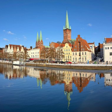 Lubeck, Almanya - 18 Şubat 2026: Karla kaplı tarihi eski bir kasaba limanı - berrak kış gökyüzü altında ortaçağ kiliseleri ve gaçalı evler ve Trave Nehri 'nin yansıttığı kuleler