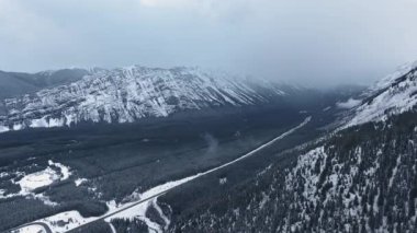 Kananaskis, Alberta, Kanada 'daki karlı kış dağlarının yamaçlarındaki kara vadiyi filme alan drone.