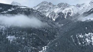 İnsansız hava aracı Kananaskis, Alberta, Kanada 'daki kış dağlarının yamaçlarına inen bir buluta doğru uçuyor.