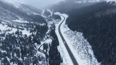 Kananaskis, Alberta, Kanada 'nın dağlık kesimlerinde donmuş bir nehrin kenarındaki yolda ilerleyen tek bir karavanın insansız hava aracı görüntüsü.
