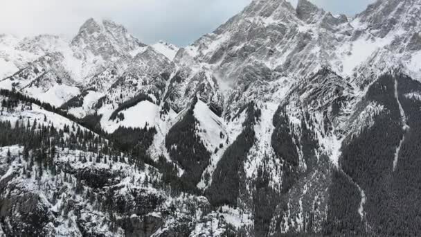Drone vliegt over de besneeuwde beboste heuvel richting de witte rotsen in de waas in de winter in Kananaskis, Alberta, Canada — Stockvideo