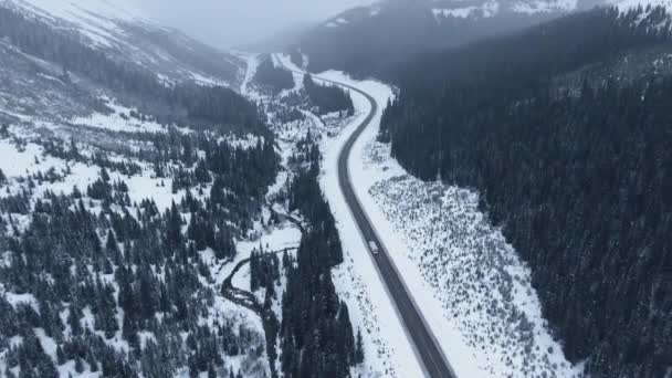 カナナスキス アルバータ州 カナダの山岳地帯を通って凍結した川の近くの道路に沿って運転する一人のトレーラーのドローンショット — ストック動画