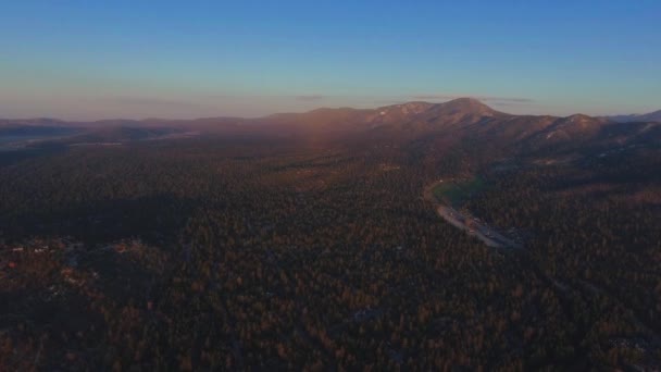 Drone dispara denso bosque, asentamiento y una montaña al atardecer cerca del Observatorio Solar Big Bear, vista aérea del Lago Big Bear, California, EE.UU. — Vídeos de Stock