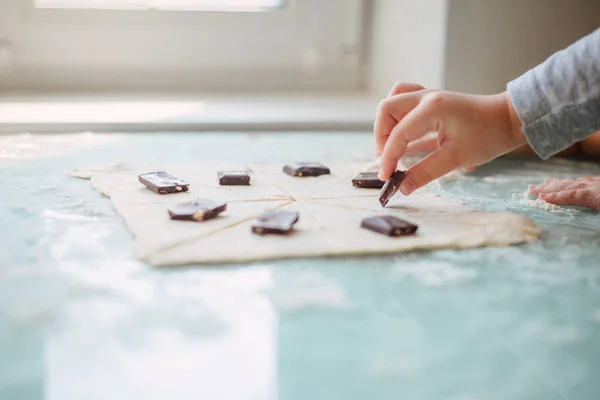 Child's hand placing pieces of chocolate on dough with flour around it