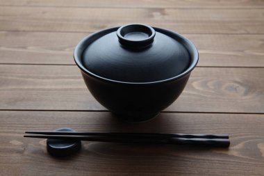 Donburi pirinç kasesi siyah ve yemek çubukları ahşap masada izole edilmiş.