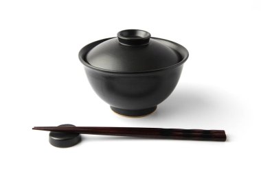 Donburi pirinç kasesi siyah ve yemek çubukları beyaz arka planda.