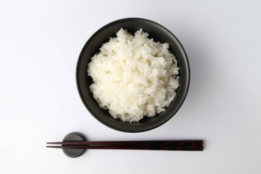 Beyaz zemin üzerinde yemek çubukları olan kasede sade beyaz pirinç.