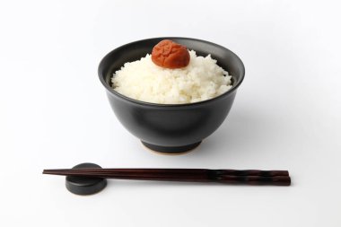 Beyaz arka planda izole edilmiş kase çubuklarıyla tuzlanmış erikli sade pirinç.