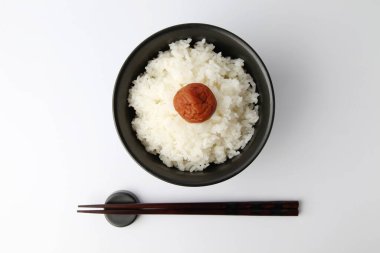 Beyaz arka planda izole edilmiş kase çubuklarıyla tuzlanmış erikli sade pirinç.