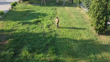 A man mows the green grass with a scythe