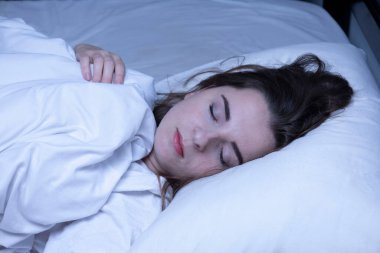Genç bir kadın, huzur içinde yatağında dinleniyor, karanlıkta derin bir uykuya dalıyor.