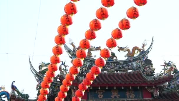 Row of red Chinese paper lanterns with ornate gold patterns and tassels. hanging on wires outside. Shot on the sky background at Buddhist temple. — Stock Video