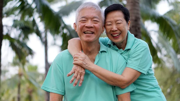 Asiatiska senior par avkopplande i parken skrattar i solsken — Stockfoto